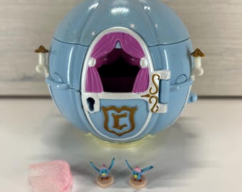 Puede incluir: Un carruaje de juguete azul claro con una llave dorada, dos figuritas de pájaros azules y un trozo de tela rosa. El carruaje tiene una puerta con un emblema dorado y cortinas rosas en el interior. El carruaje mide unos 15 cm de largo.