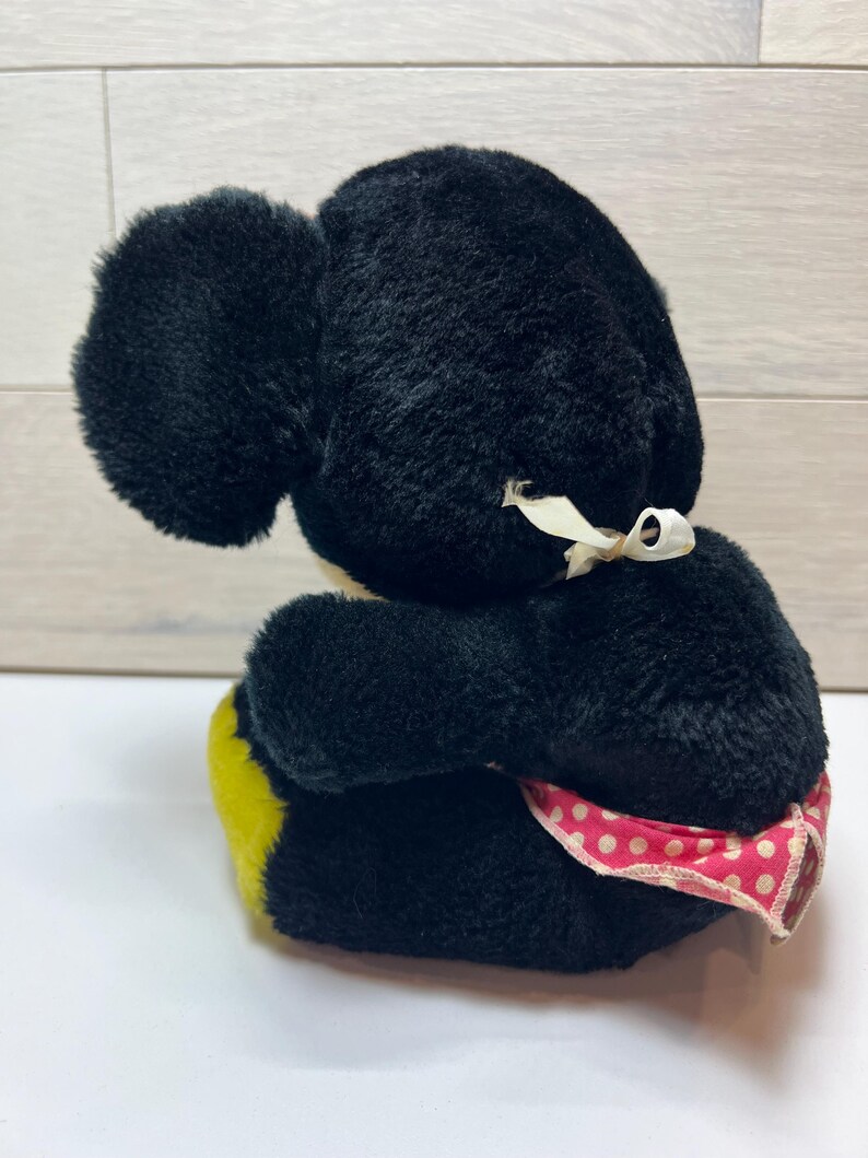 K&ouml;nnte beinhalten: Ein Vintage-Pl&uuml;schtier in Schwarz mit gro&szlig;en Ohren und einem gelb-rosa Tupfenakzent. Das Spielzeug hat ein wei&szlig;es Band um den Hals gebunden. Das Pl&uuml;schtier sitzt auf einer wei&szlig;en Oberfl&auml;che.