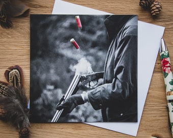 May include: A black and white photo of a person holding a shotgun with smoke coming out of the barrel. Two red shotgun shells are in the air.