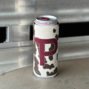 Pode incluir: Um refrigerador de latas de vaca branco e marrom com uma letra "P" de feltro bord&ocirc; na frente.