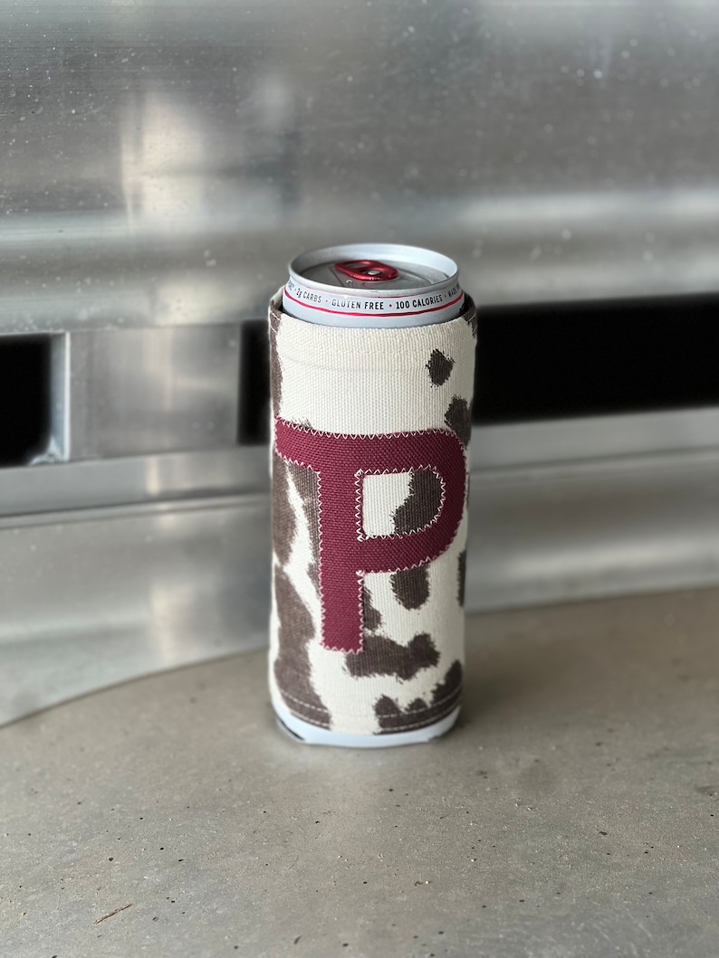 Pode incluir: Um refrigerador de latas de vaca branco e marrom com uma letra "P" de feltro bord&ocirc; na frente.