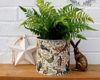 May include: A white metal tin with a colorful design of birds and text, including "Bramble Berry Fairies", is filled with a green fern plant. A white star and a bronze rabbit figurine are on a wooden surface.