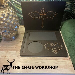 May include: A black wooden tray with a gold dragon design. The tray has a built-in cup holder and a small compartment. The tray is sitting on a wooden surface. The text "THE CHASE WORKSHOP" is visible on the surface.