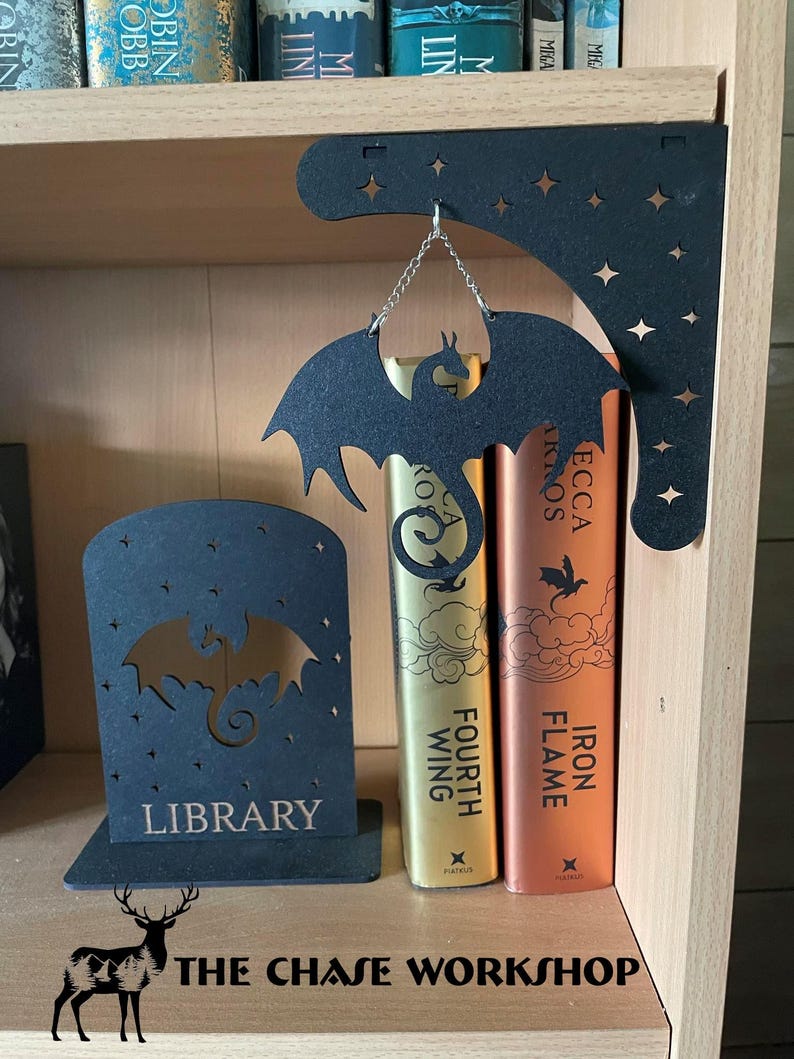 May include: Black metal dragon bookends with a star-shaped design and the word "LIBRARY" on the front. A black metal dragon hanging from a shelf with the words "IRON FLAME" and "FOURTH WING" on the books.