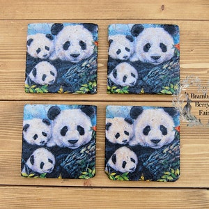 May include: Set of four square black slate coasters featuring a printed image of a panda family. The image depicts a mother panda and two cubs against a blue and green background.