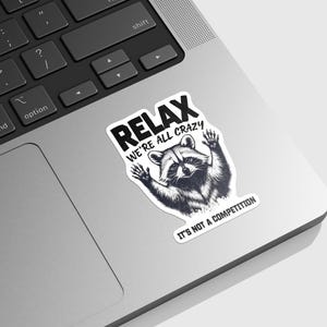 May include: A black and white sticker with a raccoon and the text "Relax We're All Crazy It's Not A Competition".