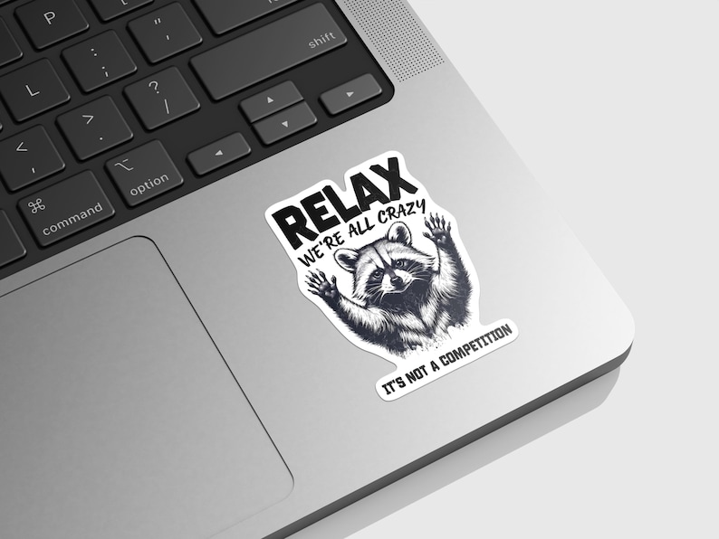 May include: A black and white sticker with a raccoon and the text "Relax We're All Crazy It's Not A Competition".