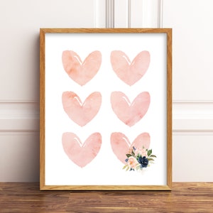 May include: A printable wall art design featuring six pink watercolour hearts, with one heart accented with a floral bouquet in shades of blue and pink.