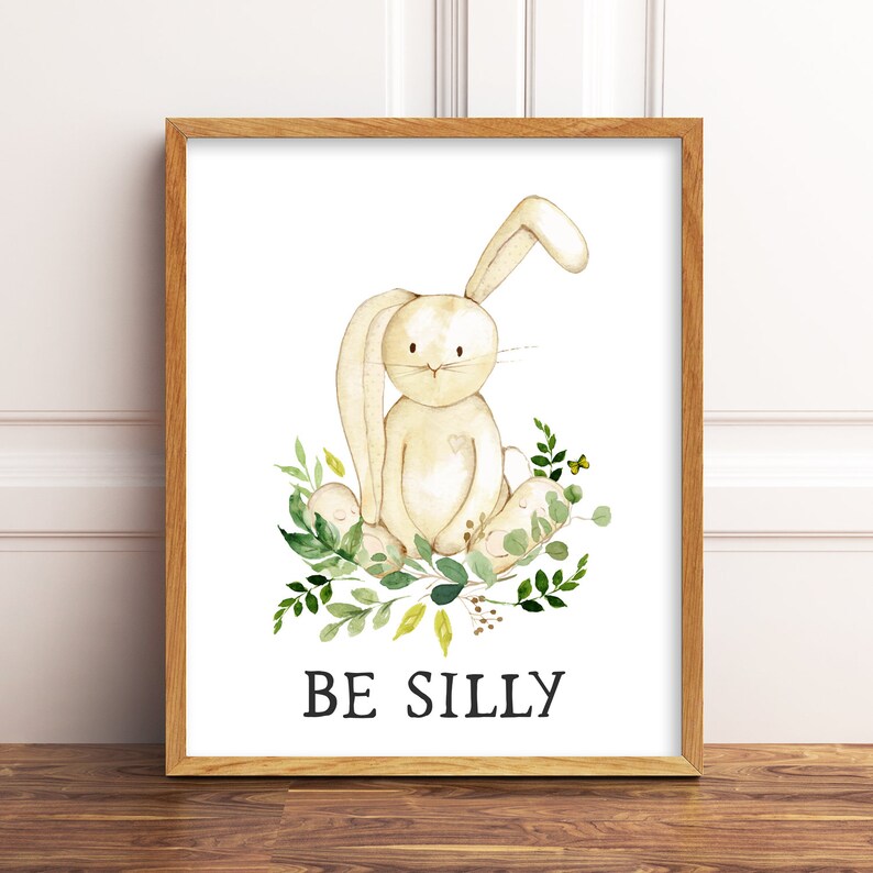 May include: A watercolor illustration of a white bunny sitting on a bed of green leaves with yellow flowers. The text "BE SILLY" is printed below the bunny.