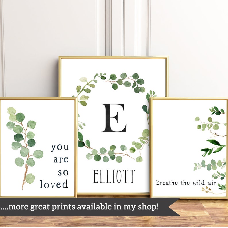May include: Three framed prints with a watercolor eucalyptus wreath design. The first print features the letter "E" in a wreath with the name "ELLIOTT" below. The second print has a wreath with the text "you are so loved". The third print has a wreath with the text "breathe the wild air".