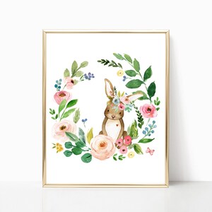 Puede incluir: Una ilustraci&oacute;n de acuarela de un conejito marr&oacute;n con una corona de flores, rodeado de una corona de flores rosas, blancas y amarillas y hojas verdes.