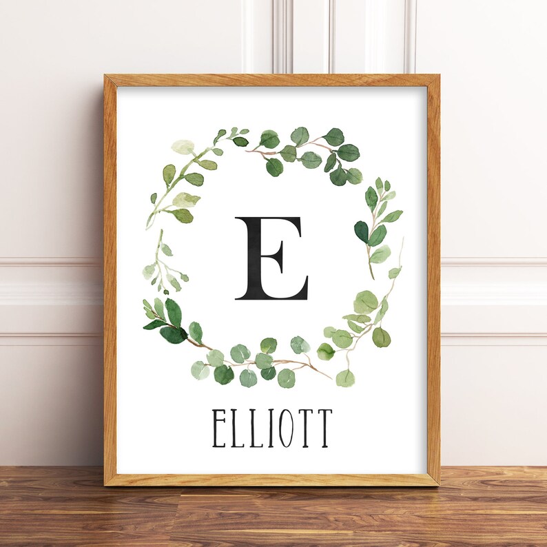 May include: A framed print with a watercolor illustration of a green eucalyptus wreath with the letter "E" in the center and the name "ELLIOTT" below.