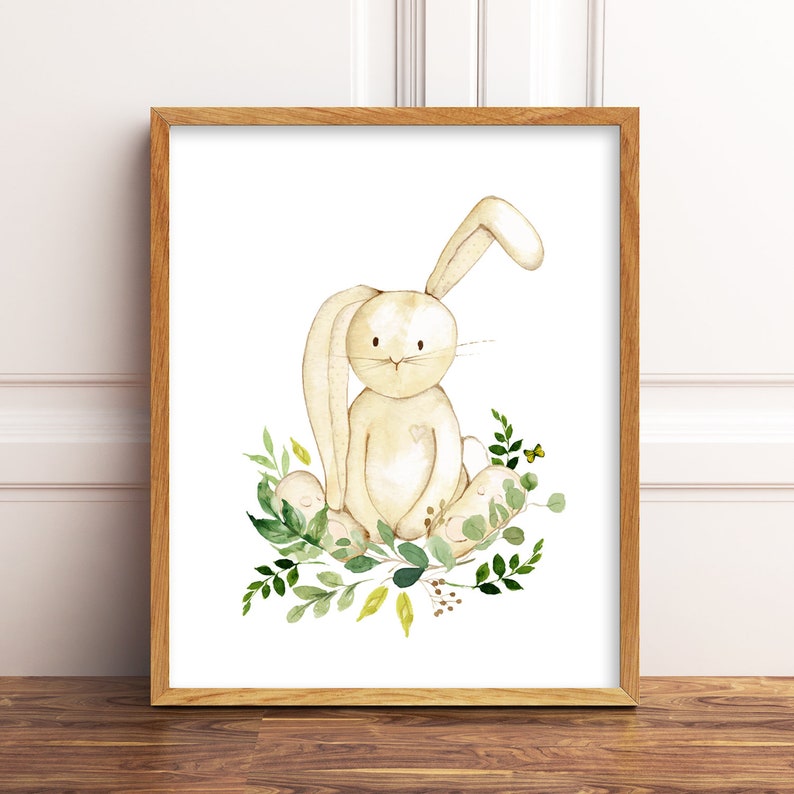 May include: A watercolour illustration of a beige bunny sitting on a bed of green leaves. The bunny has a small heart on its chest and is surrounded by green leaves and small yellow flowers.