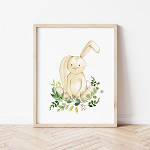 K&ouml;nnte beinhalten: Eine Aquarell-Illustration eines beigefarbenen Kaninchens, das in einem Bett aus gr&uuml;nen und gelben Bl&auml;ttern sitzt. Das Kaninchen hat ein langes, schlaffes Ohr und einen s&uuml;&szlig;en Ausdruck.