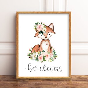 May include: A watercolor illustration of a fox wearing a pink flower crown. The fox is sitting on a bed of pink and white flowers. The text "be clever" is written below the fox.