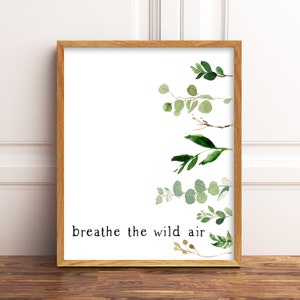 Könnte beinhalten: Ein gerahmter Druck mit weißem Hintergrund und einer Aquarell-Illustration von grünen Blättern und Zweigen. Der Text "breathe the wild air" ist in Schwarz am unteren Rand des Drucks gedruckt.
