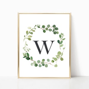 May include: A printable art print featuring a watercolor wreath of green leaves with a black letter W in the center. The print is framed in a gold frame.
