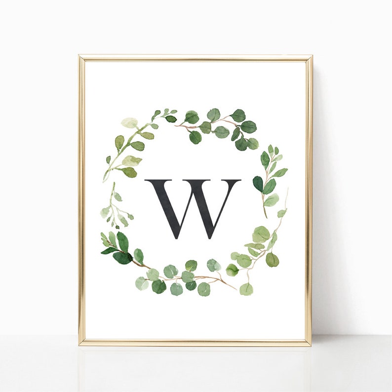 May include: A printable art print featuring a watercolor wreath of green leaves with a black letter W in the center. The print is framed in a gold frame.