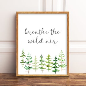 May include: Wooden framed art print with the text "breathe the wild air" in black script. The bottom of the print features a watercolor illustration of green pine trees. The frame is a light brown color.