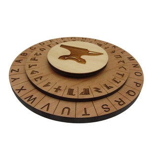 May include: A wooden cipher wheel with three concentric circles. The outer two circles feature engraved letters and symbols. The center circle has an engraved anvil symbol. The wood has a light brown color.