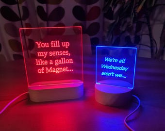 May include: Two illuminated signs with text. The red sign says "You fill up my senses, like a gallon of Magnet..." The blue sign says "We're all Wednesday aren't we..."