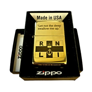 Puede incluir: Un encendedor Zippo dorado con un emblema de la Royal Navy negro y dorado y la inscripci&oacute;n 'Let not the deep swallow me up.' El encendedor est&aacute; en su caja original.