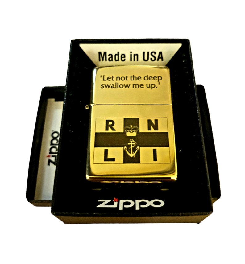 Puede incluir: Un encendedor Zippo dorado con un emblema de la Royal Navy negro y dorado y la inscripci&oacute;n 'Let not the deep swallow me up.' El encendedor est&aacute; en su caja original.