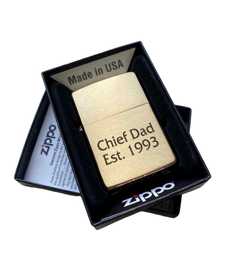 Puede incluir: Un encendedor Zippo dorado con la inscripci&oacute;n "Chief Dad Est. 1993" en una caja negra.