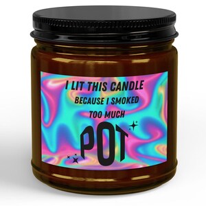 Può includere: Un barattolo per candela in vetro marrone con coperchio nero e un'etichetta rettangolare con uno sfondo olografico a vortici rosa e blu. L'etichetta riporta il testo nero: I LIT THIS CANDLE BECAUSE I SMOKED TOO MUCH POT, arricchito da piccole icone a forma di stella.