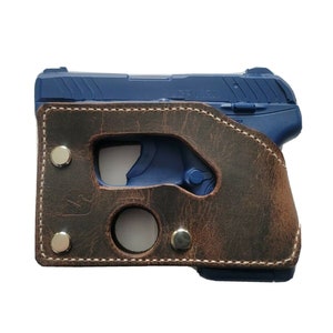 May include: A brown leather holster with a stitched edge and silver rivets. The holster is designed to hold a small, blue handgun.