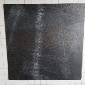 Op de afbeelding: Een zwart vierkant vel van getextureerd materiaal met witte strepen.