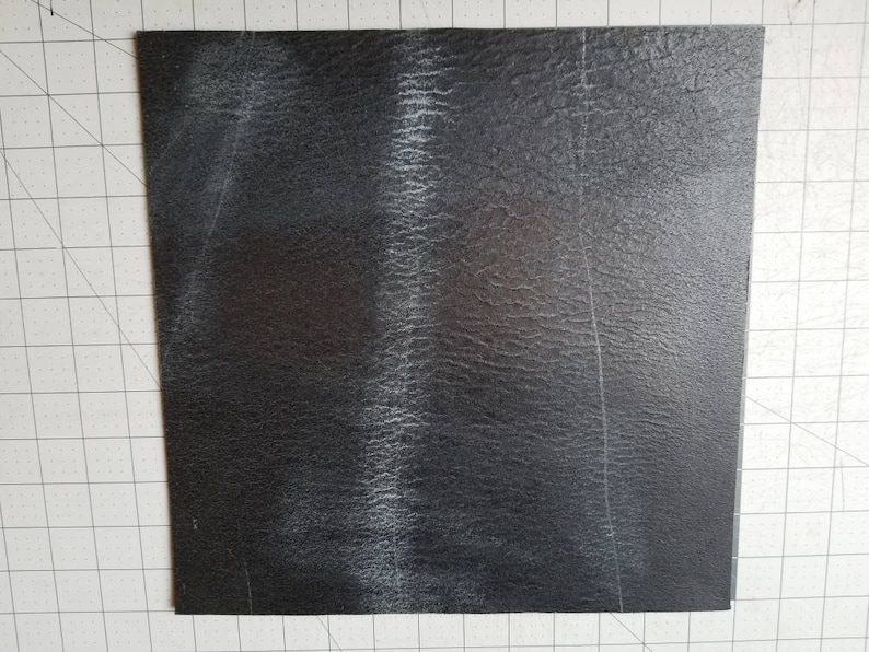 Op de afbeelding: Een zwart vierkant vel van getextureerd materiaal met witte strepen.