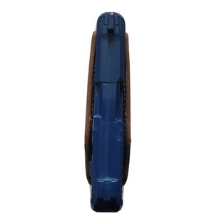 Puede incluir: Una pistola azul en una funda de cuero marr&oacute;n. El arma es de color azul s&oacute;lido y est&aacute; parcialmente encerrada en la funda. La funda es de color marr&oacute;n oscuro y parece ser de cuero.