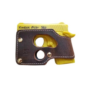 May include: A yellow Kimber Micro 380 handgun in a brown leather holster. The holster is secured with brass rivets and white stitching. The text "Kimber Micro 380" is visible on the handgun.