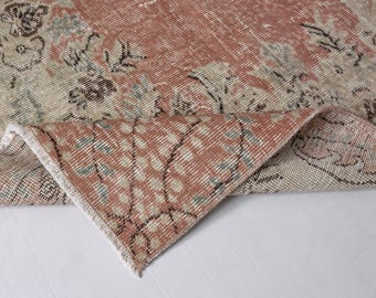 May include: A close-up of a pink and beige patterned rug with a fringed edge. The rug is folded in half, revealing the underside.