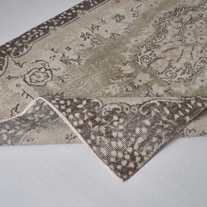 Puede incluir: Una alfombra vintage con fondo beige y estampado floral marrón. La alfombra está doblada por la mitad, mostrando la parte inferior de la alfombra.