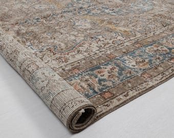 May include: Rolled-up area rug with a distressed, vintage look. The rug features a complex floral pattern in shades of beige, brown, and blue. The edges are bordered with a darker brown and blue design. The rug is on a white surface.