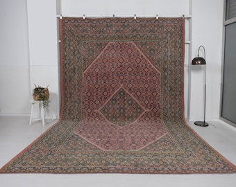 May include: Large, rectangular rug with an intricate floral and geometric pattern in shades of pink, green, and brown. The rug features a central diamond-shaped design and a detailed border. The rug is displayed on a white surface.