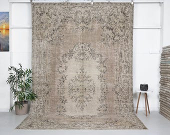 May include: A large, rectangular, beige rug with an intricate floral pattern in shades of brown and black. The rug features a central medallion design and a distressed, vintage appearance, suitable for home decor.