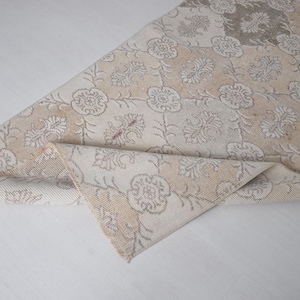 May include: A white and beige rug with a floral pattern. The rug is folded in half and the pattern is visible on both sides.