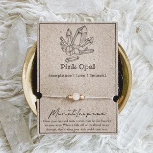Peut inclure: Un bracelet en cristal d'opale rose sur une carte brune avec le texte "Pink Opal Acceptance | Love | Renewal" et "Fermez les yeux et faites un vœu, puis attachez ce bracelet à votre poignet. Lorsqu'il tombera ou que le fil s'usera, c'est à ce moment-là que votre souhait pourrait se réaliser."