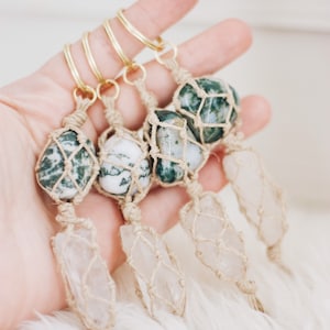 May include: Four keychains with green and white agate stones wrapped in macrame and attached to gold key rings. Each stone is attached to a white crystal point also wrapped in macrame.
