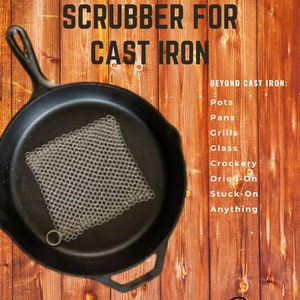May include: A cast iron skillet with a chainmail scrubber. The image has text that reads "BEST CHAINMAIL SCRUBBER FOR CAST IRON" and "THE SCRUFFER". The background is a wooden surface.