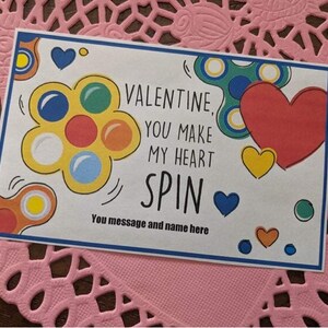 May include: A Valentine's Day card with a colorful fidget spinner design. The card says "Valentine, you make my heart spin".