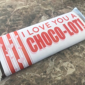 May include: A white chocolate bar wrapper with red and white stripes and pink hearts. The wrapper has the text "I love you a Choco-lot!" printed on it.