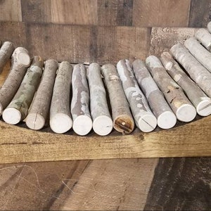 May include: A wooden pet bed with a curved shape and a base made of natural wood. The bed is filled with a row of smooth, white-painted branches.