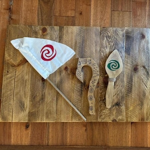 May include: A white flag with a red spiral design, a wooden hook, and a wooden spoon with a green spiral design. The items are arranged on a wooden surface.