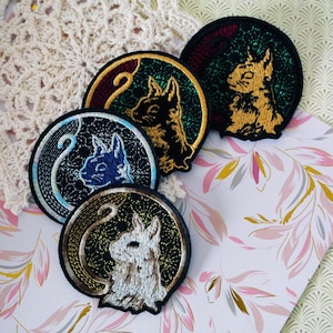 May include: Embroidered patches featuring a rabbit design in various colors: black, gold, blue, and white. Each patch is circular with a detailed rabbit illustration and a decorative border. The patches are on a floral patterned background.