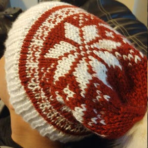 May include: A red and white knitted beanie with a pom pom. The beanie has a snowflake pattern.
