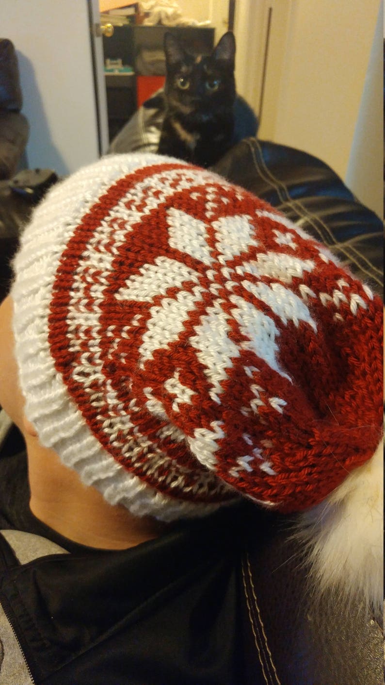 May include: A red and white knitted beanie with a pom pom. The beanie has a snowflake pattern.